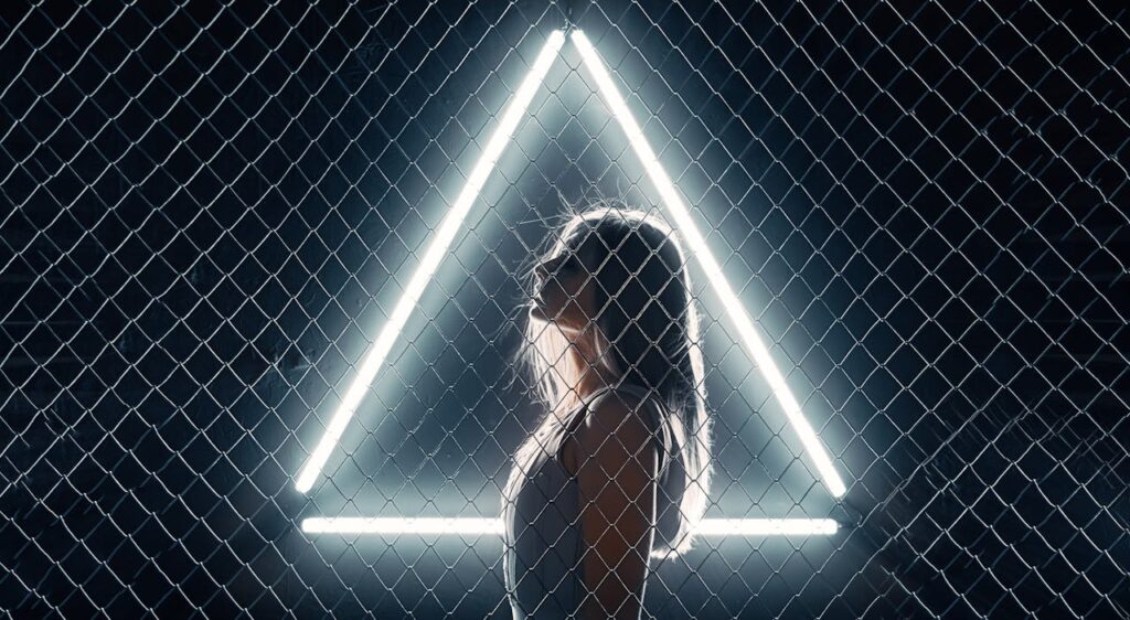 Demo Post 2 Side profile of a woman behind a chain-link fence with a glowing triangle, creating a striking silhouette.