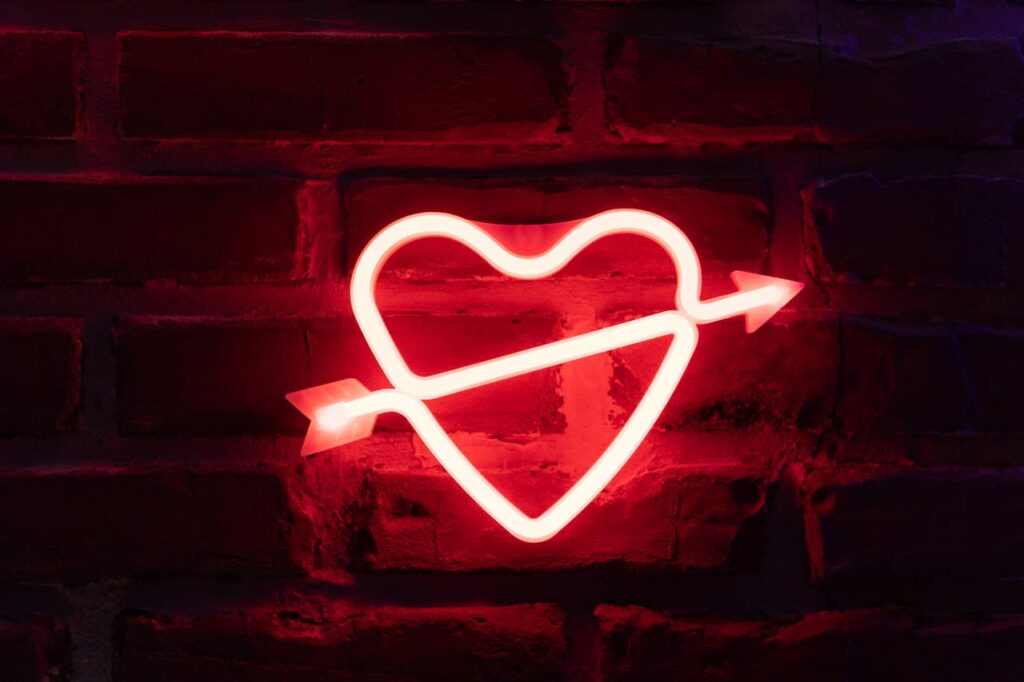 Demo Post 3 Glowing neon heart with arrow on a dark brick wall, romantic and vibrant.